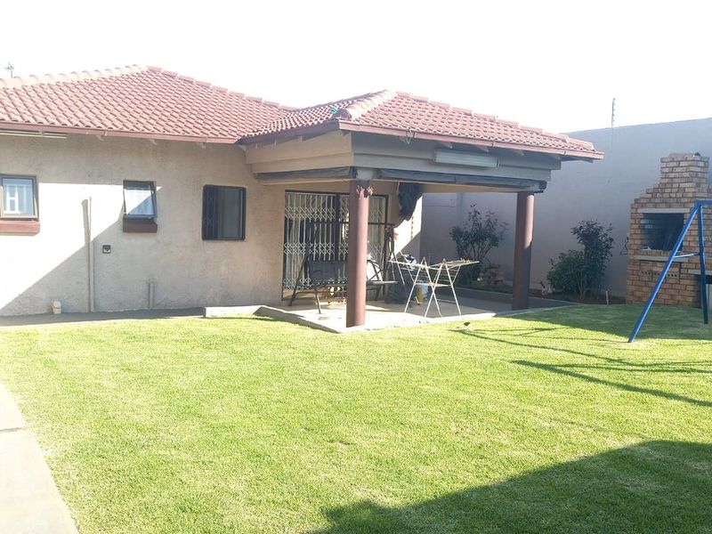 Rear view of the house featuring a covered patio, a brick built-in braai, and a well-maintained lawn area.