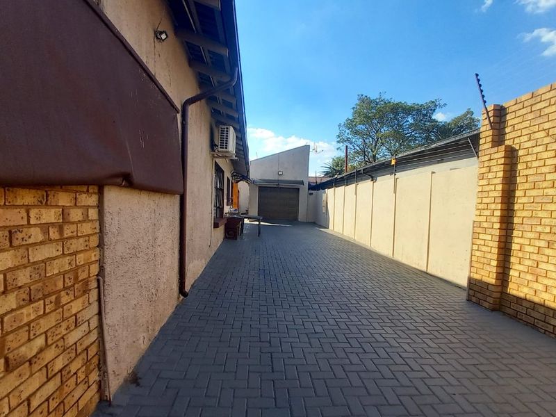 A paved side driveway leading to a rear garage, featuring brick boundary walls with electric fencing and an external air conditioning unit.