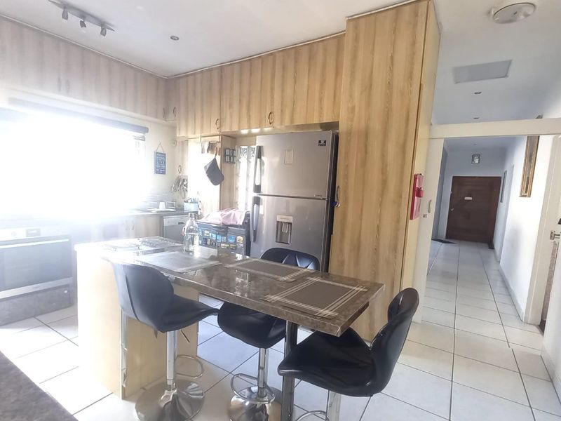A functional kitchen featuring light wood cabinetry, stone countertops with an integrated breakfast bar, and tiled flooring, leading into a hallway.