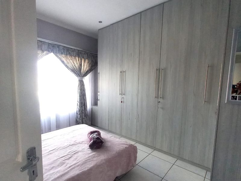 A bedroom featuring light wood-finish built-in cupboards, tiled flooring, and recessed ceiling lighting.