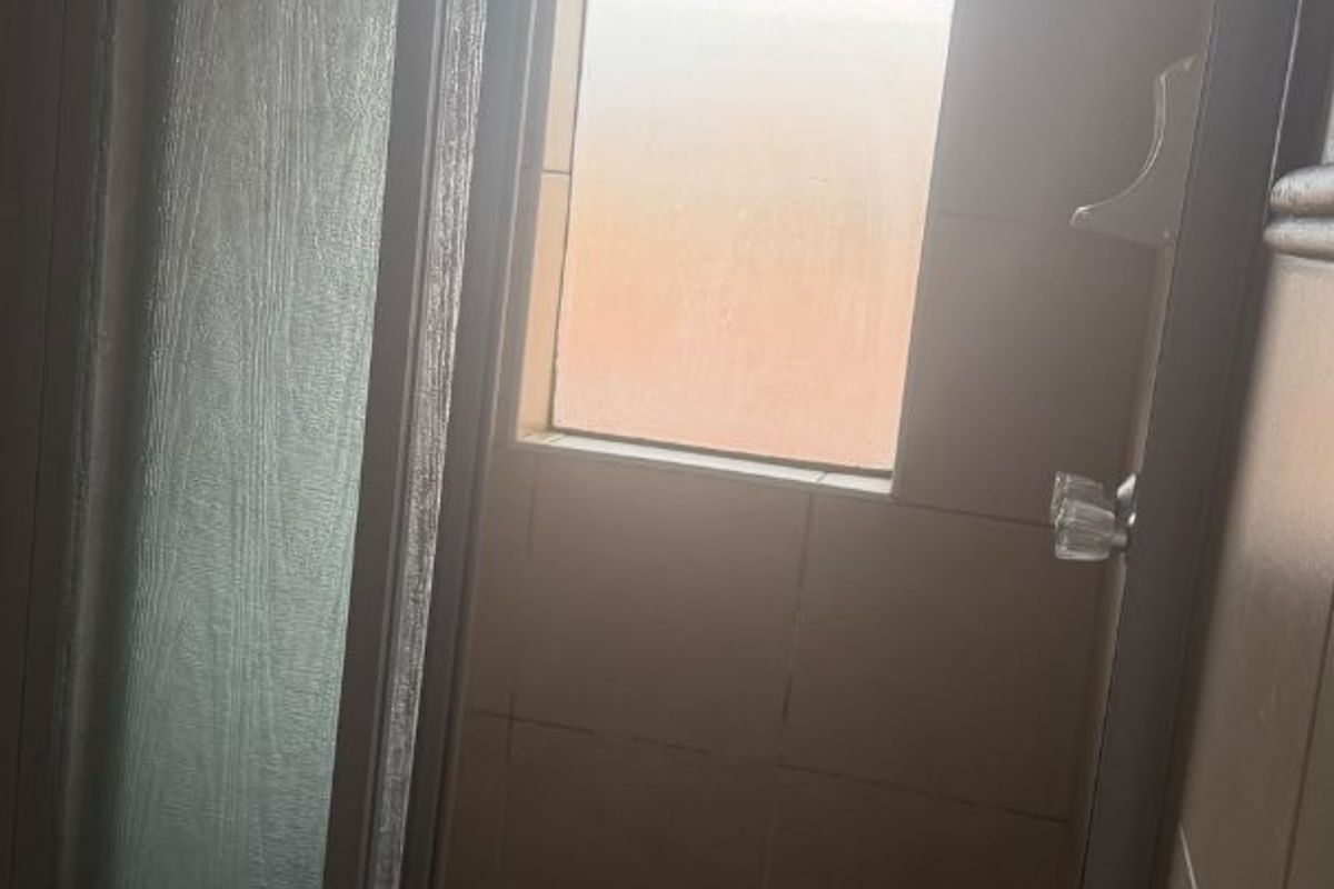 A compact shower stall featuring tiled walls, a framed glass door, and a small window, requiring some maintenance and updates.
