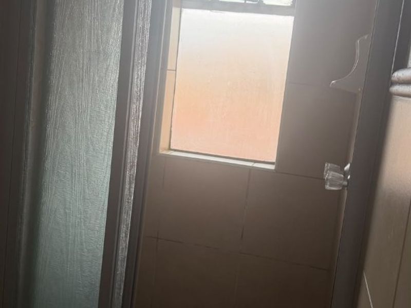 A compact shower stall featuring tiled walls, a framed glass door, and a small window, requiring some maintenance and updates.