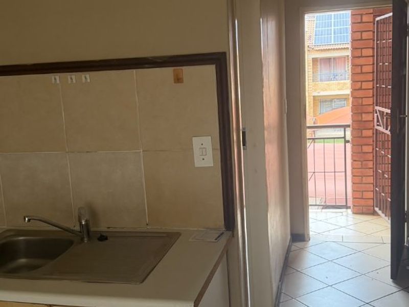 A compact kitchen area featuring basic cabinetry, a stainless steel sink, and tiled flooring, with direct access to an outdoor balcony area.