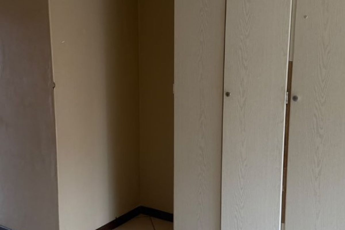 An empty bedroom featuring tiled flooring and built-in cupboards with a dated finish, offering a blank canvas for potential renovation or restyling.