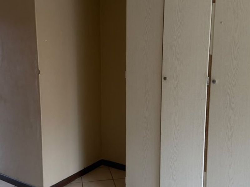An empty bedroom featuring tiled flooring and built-in cupboards with a dated finish, offering a blank canvas for potential renovation or restyling.