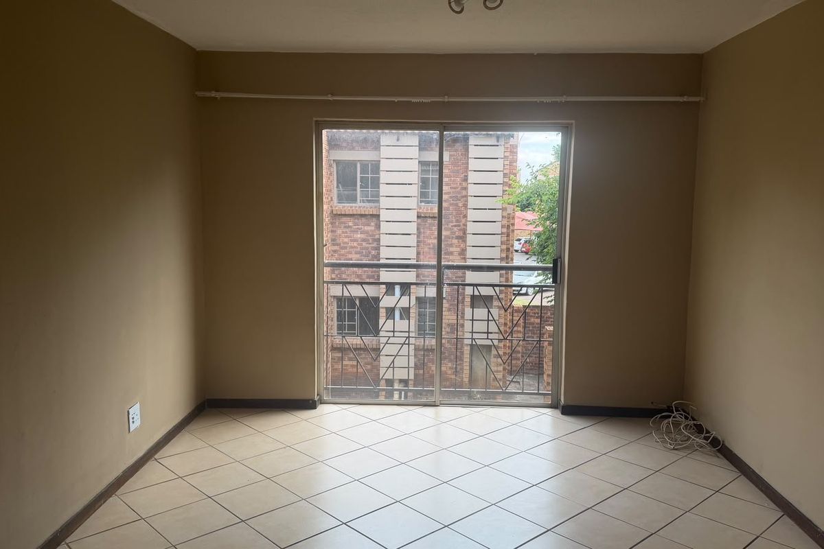 An empty living room featuring tiled flooring and a sliding glass door with a security gate, providing access to the exterior.