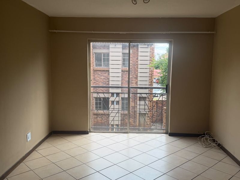 An empty living room featuring tiled flooring and a sliding glass door with a security gate, providing access to the exterior.