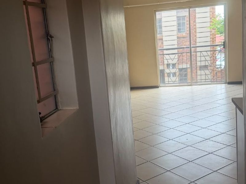 A vacant hallway with tiled flooring leading towards a sliding glass door with a security gate, showing signs of wear on the ceiling and walls.