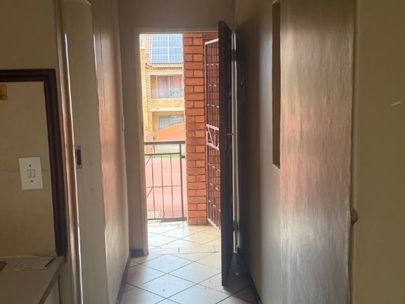 A functional hallway featuring tiled flooring and a security gate leading to an outdoor balcony area.