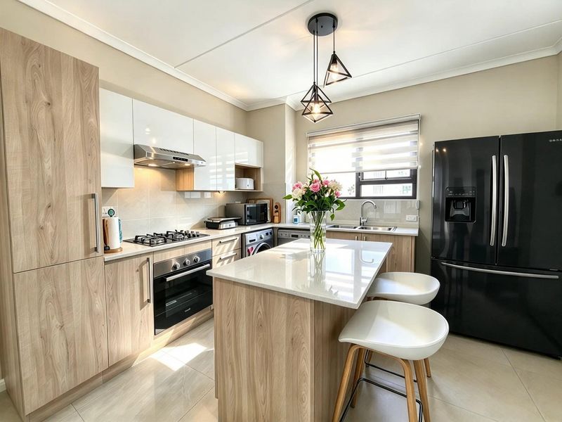 Modern kitchen featuring light wood cabinetry, stone countertops, a central island, gas hob, and integrated appliances in a bright, well-maintained space.