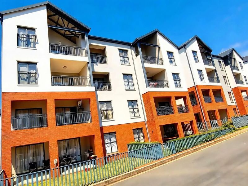 A multi-story apartment complex featuring a combination of brick and rendered facade, private balconies with metal railings, and secure perimeter fencing.