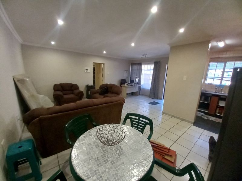 Open-plan living and dining area featuring ceramic floor tiles, recessed downlighting, and an adjacent kitchen space.