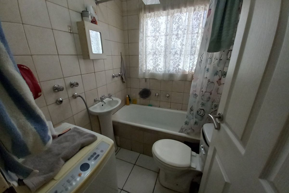 A compact bathroom featuring a pedestal basin, bathtub with shower head, and toilet, finished with tiled walls and flooring.
