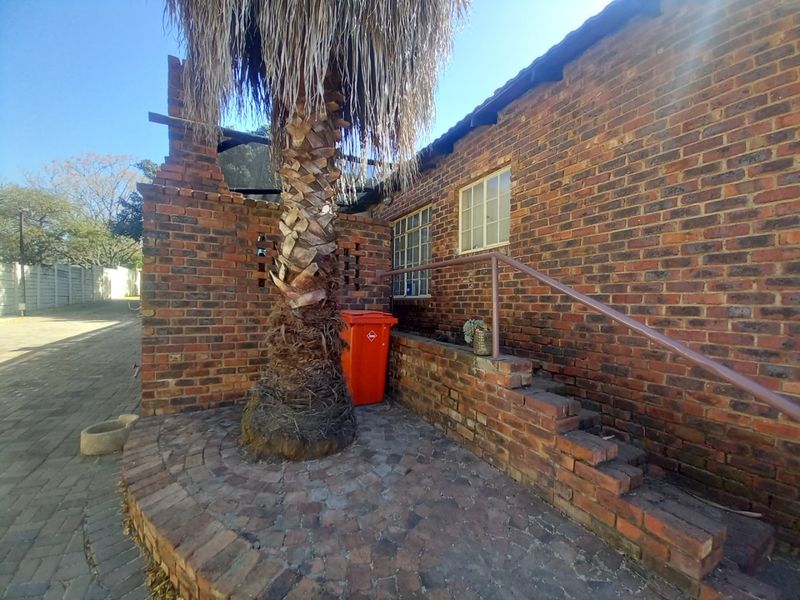 Rear exterior view of the apartment featuring a face brick facade, paved patio area, and brick steps with a metal handrail.