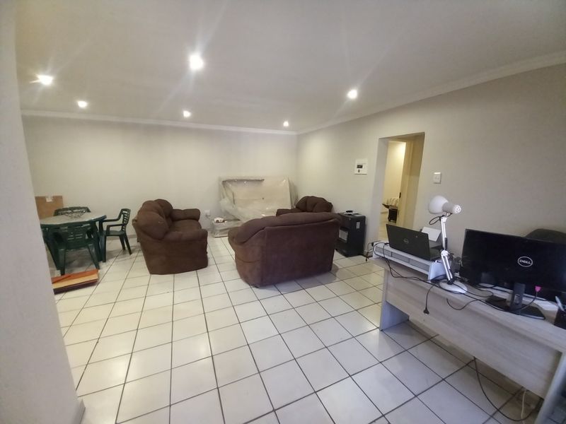 An open-plan living area featuring white tiled flooring, recessed downlighting, and coved ceiling cornices, providing a versatile space for living and dining arrangements.