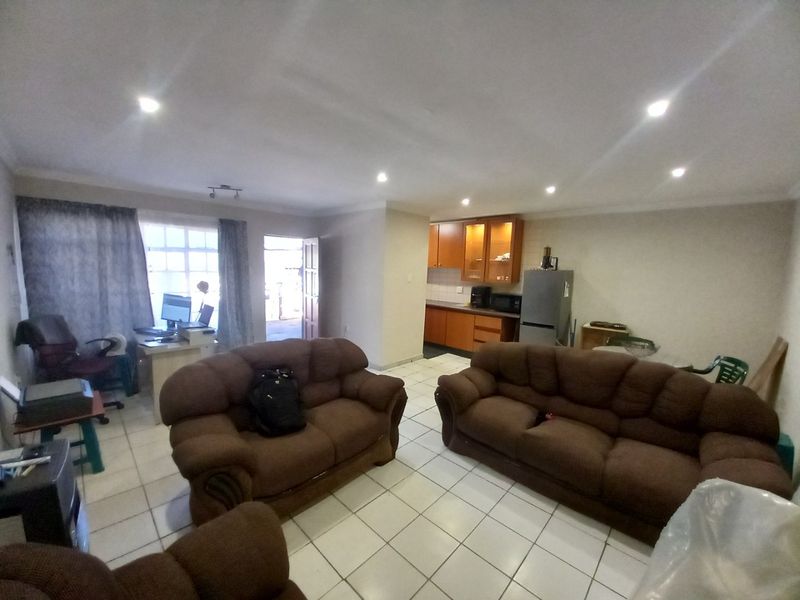 Open-plan living area featuring tiled flooring, recessed lighting, and a functional kitchen with wooden cabinetry and laminate countertops.