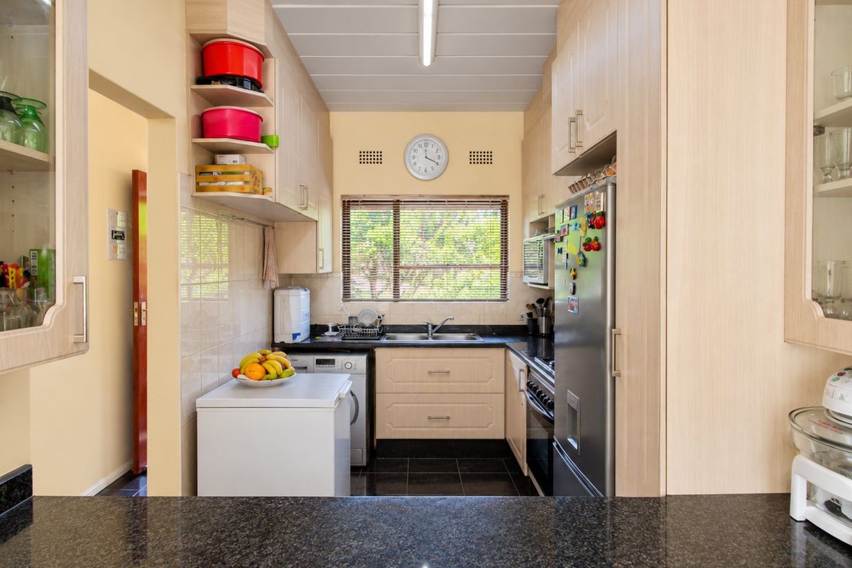 A functional kitchen featuring light wood-tone cabinetry, dark granite countertops, a double basin sink, and integrated appliances with tiled finishes.