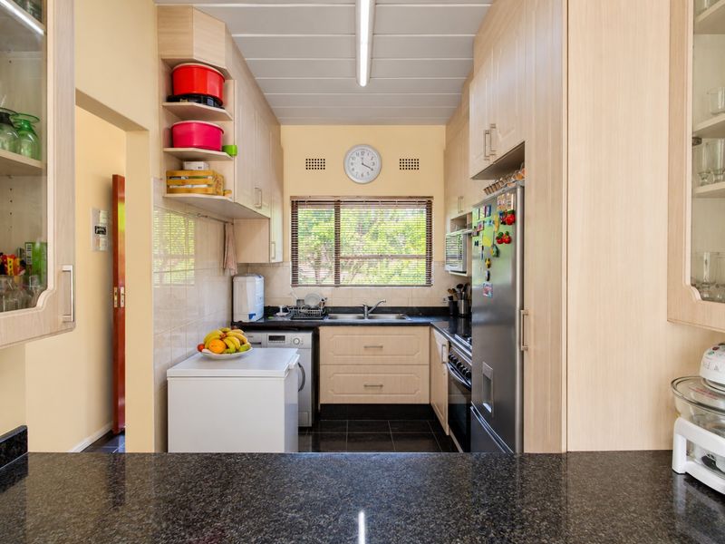 A functional kitchen featuring light wood-tone cabinetry, dark granite countertops, a double basin sink, and integrated appliances with tiled finishes.