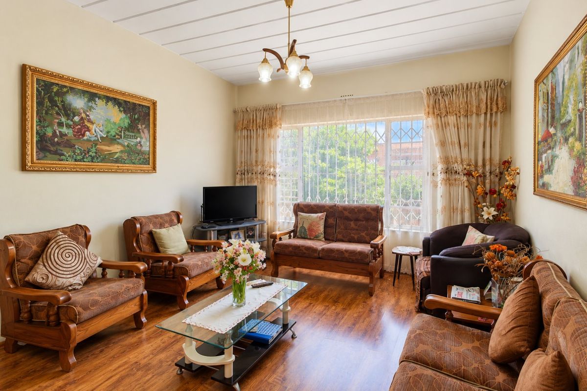 A well-maintained living room featuring laminate flooring, a large window with security bars, and a central ceiling light fixture.