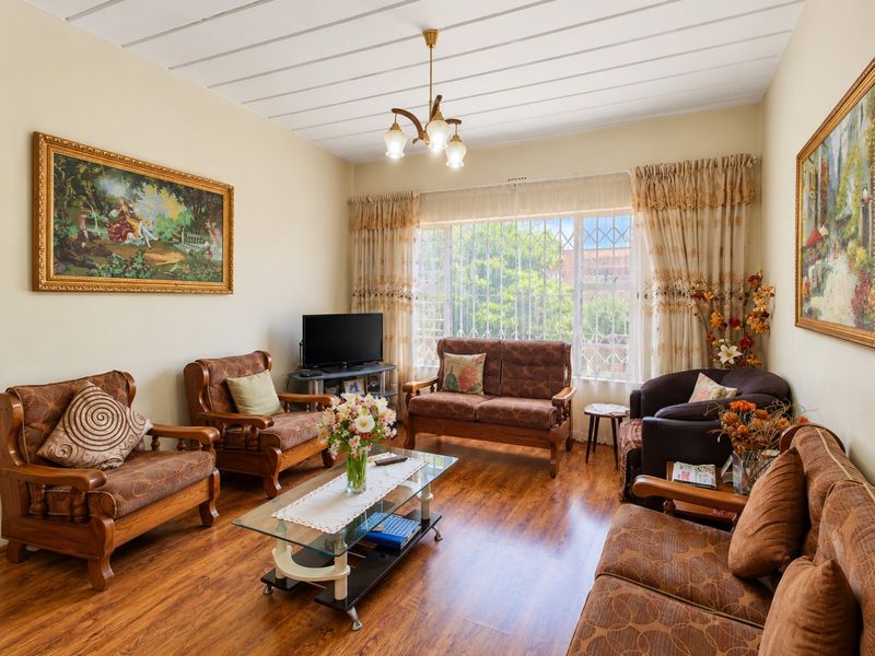 A well-maintained living room featuring laminate flooring, a large window with security bars, and a central ceiling light fixture.
