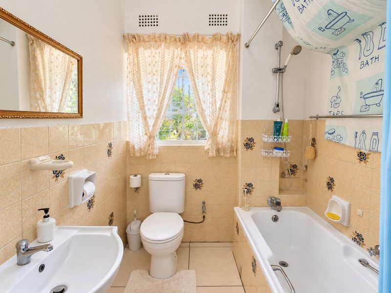 A functional bathroom featuring a pedestal basin, toilet, and bathtub with shower mixer, finished with dated floral-patterned ceramic wall tiles.