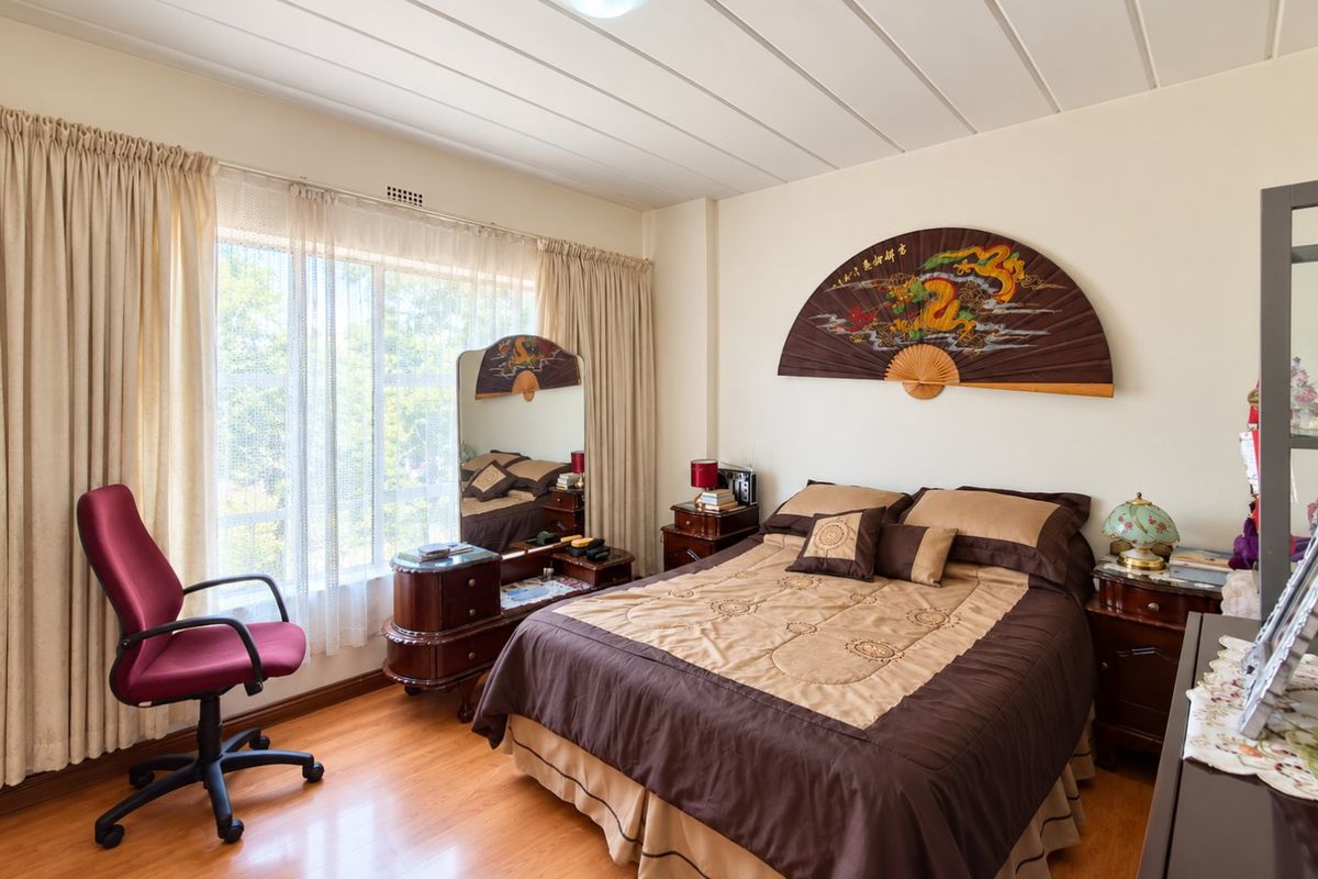 A well-maintained bedroom featuring laminate flooring, large windows with curtain tracks, and a functional ceiling light fixture.