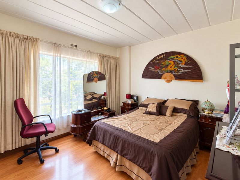A well-maintained bedroom featuring laminate flooring, large windows with curtain tracks, and a functional ceiling light fixture.