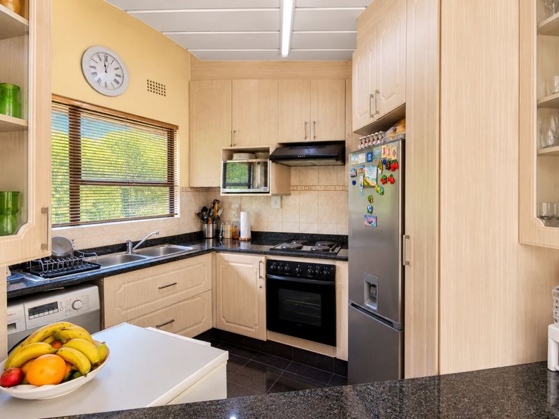 A functional kitchen featuring light wood cabinetry, granite countertops, a built-in oven and hob, and a double basin sink with a window view.