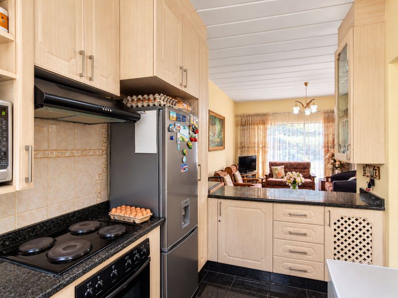 Open-plan kitchen featuring light wood cabinetry, granite countertops, and integrated appliances, flowing into a comfortable living area with natural light.