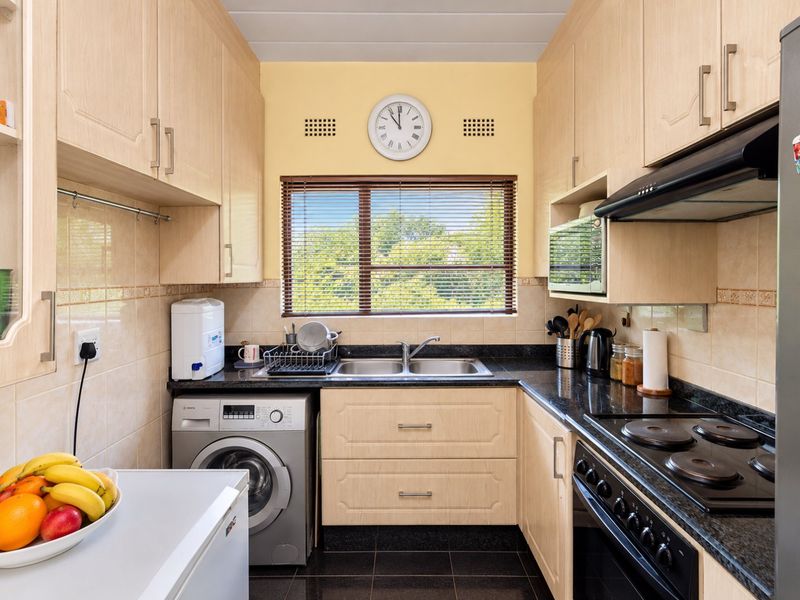 Compact kitchen featuring light wood cabinetry, dark granite countertops, tiled backsplash, and integrated laundry facilities with a view through the window.