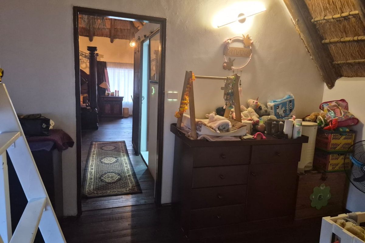Bedroom featuring a traditional thatched roof with exposed timber rafters and dark wood flooring, providing a rustic aesthetic with direct access to an adjacent room.