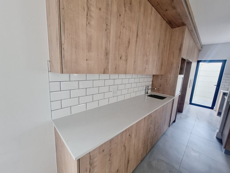 Modern kitchen featuring wood-look cabinetry, white subway tile backsplash, stone countertops, and an undermount sink with a sleek mixer tap.