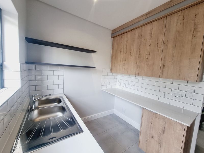 A modern, clean scullery featuring wood-look cabinetry, stone countertops, a double bowl stainless steel sink, and a classic white subway tile backsplash.