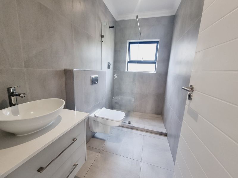 Modern bathroom featuring a wall-hung toilet, glass shower enclosure, and a sleek vanity with a vessel sink, finished with contemporary grey wall and floor tiles.