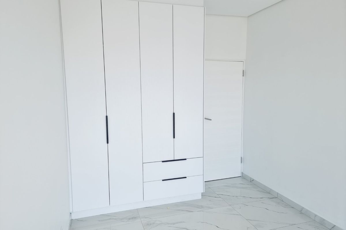 A clean, modern bedroom featuring white built-in cupboards, marble-look tiled flooring, and recessed lighting, presenting a bright and neutral space.