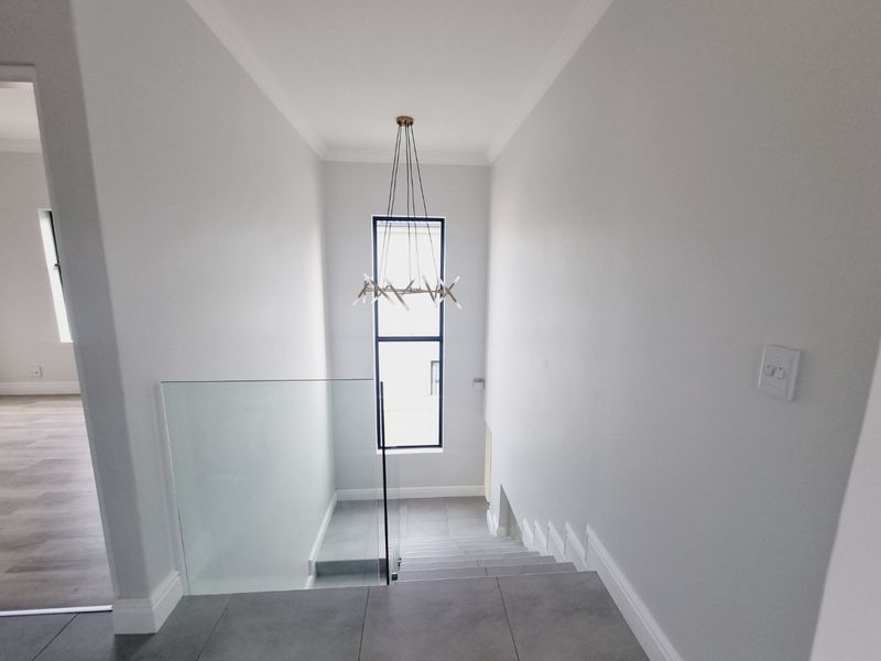 A bright, modern hallway featuring a glass balustrade, tiled staircase, and a contemporary pendant light fixture.