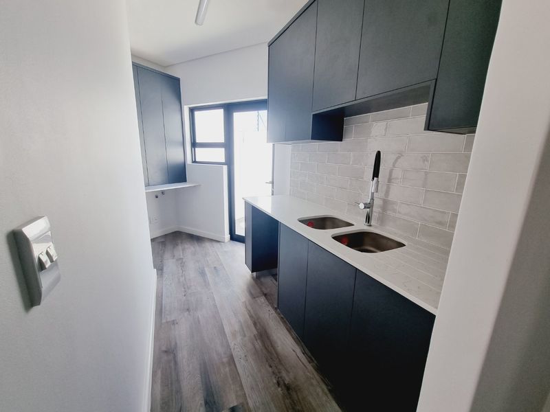 Modern scullery featuring dark cabinetry, stone countertops, double stainless steel sink, subway tile backsplash, and durable laminate flooring with direct outdoor access.