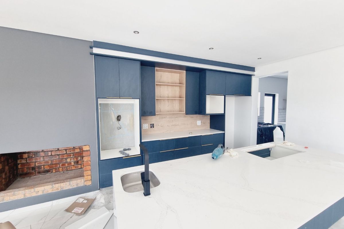 Modern kitchen under construction featuring a large island with stone countertop, dark blue cabinetry, and an integrated brick fireplace in an open-plan layout.