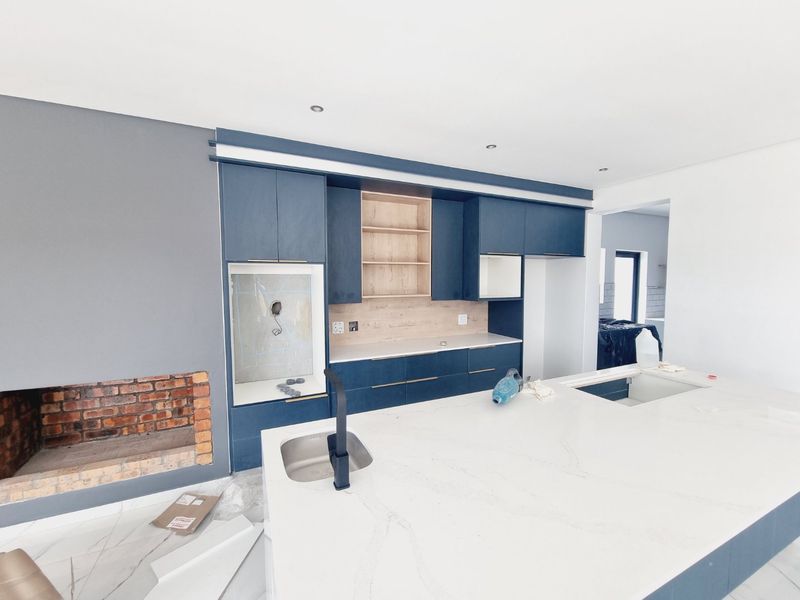 Modern kitchen under construction featuring a large island with stone countertop, dark blue cabinetry, and an integrated brick fireplace in an open-plan layout.