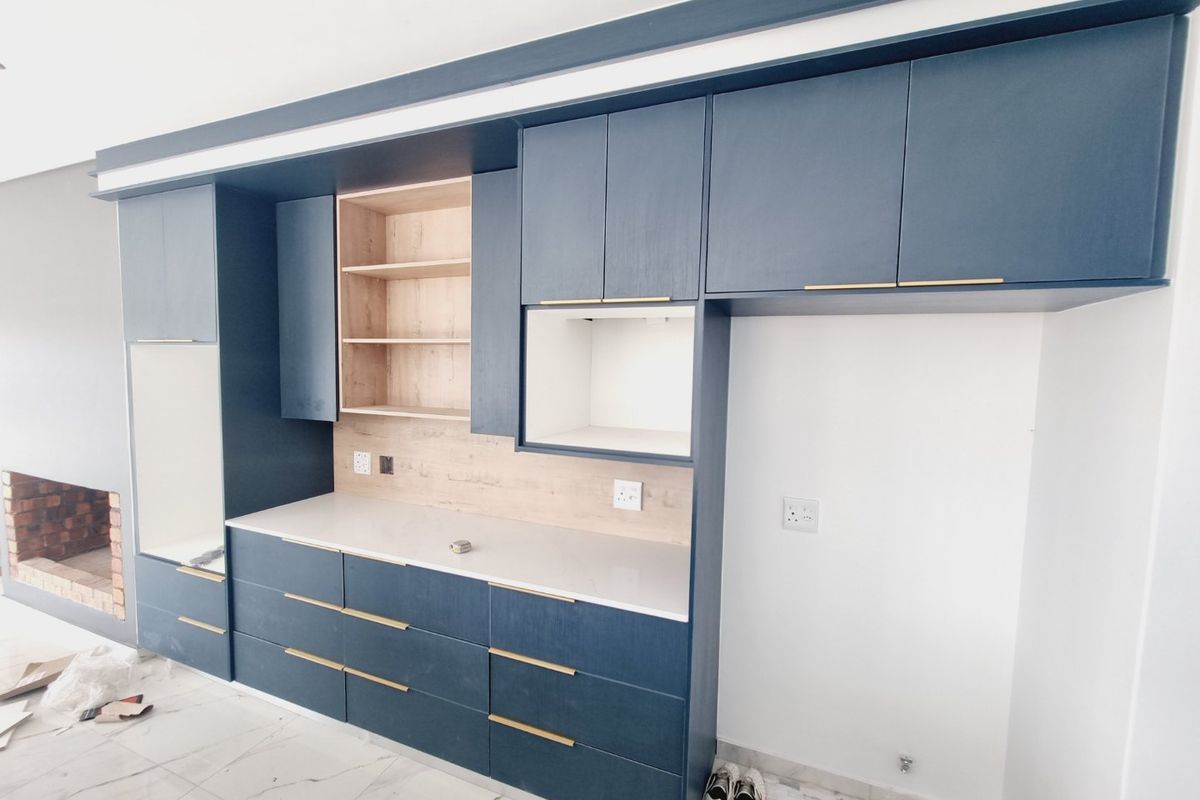 Modern kitchen featuring navy blue cabinetry, light wood accents, stone countertops, and an integrated fireplace, presenting a clean and contemporary aesthetic.