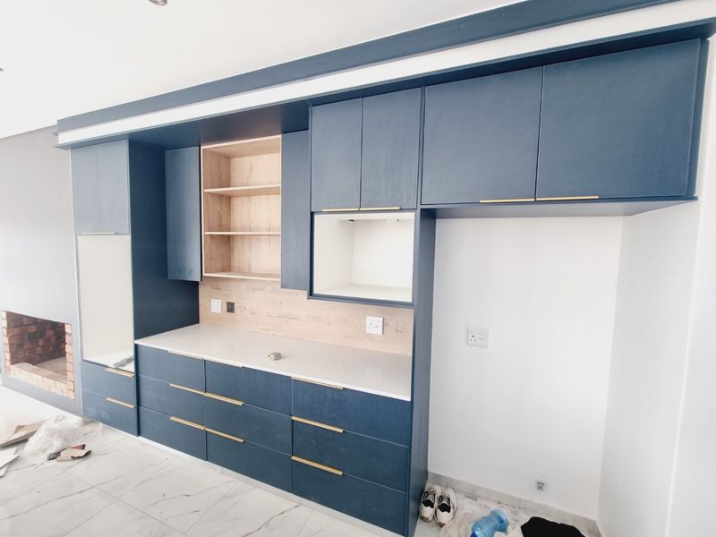 Modern kitchen featuring navy blue cabinetry, light wood accents, stone countertops, and an integrated fireplace, presenting a clean and contemporary aesthetic.