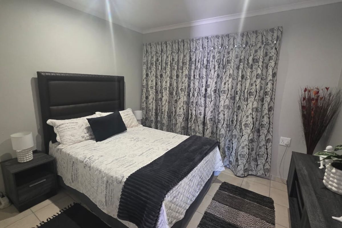A well-maintained bedroom featuring neutral wall tones, tiled flooring, and full-length window treatments.