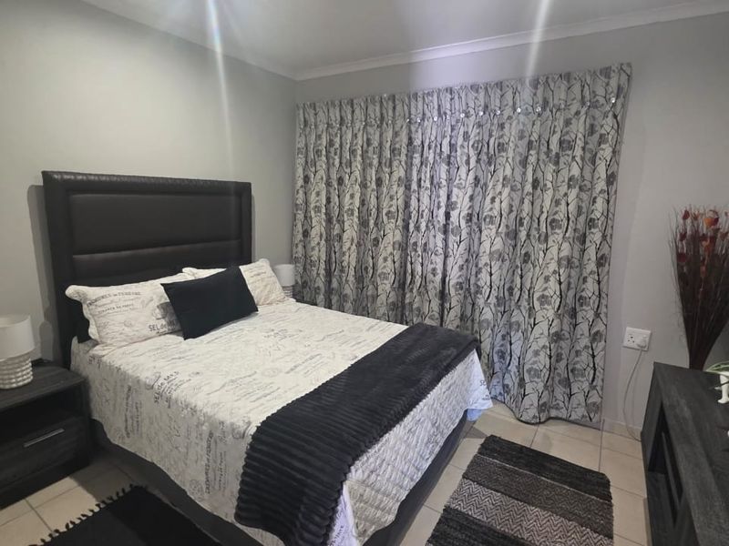 A well-maintained bedroom featuring neutral wall tones, tiled flooring, and full-length window treatments.