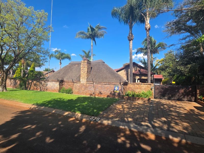 Front exterior view of a property featuring a brick boundary wall, thatched roof, paved driveway, and established garden landscaping.