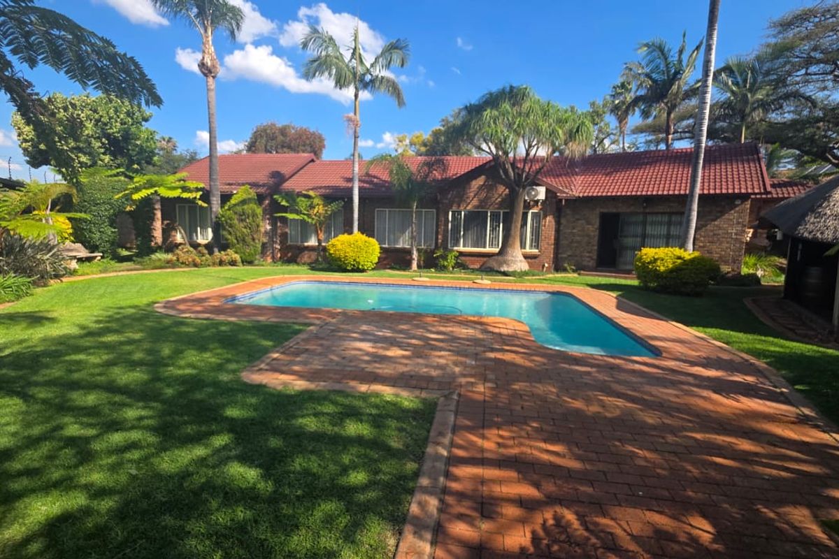 Spacious rear garden featuring a well-maintained swimming pool, brick paved patio area, and established landscaping with a view of the main house facade.