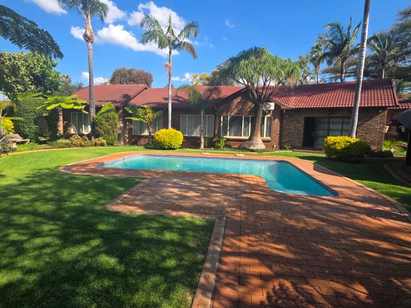 Spacious rear garden featuring a well-maintained swimming pool, brick paved patio area, and established landscaping with a view of the main house facade.