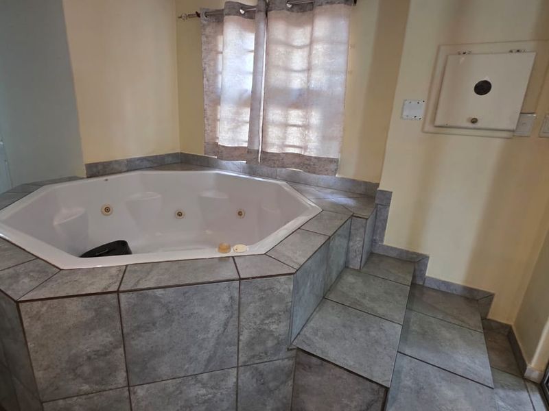 A bathroom featuring a built-in corner bathtub with grey tiled surround and matching floor tiles, providing a functional space for relaxation.