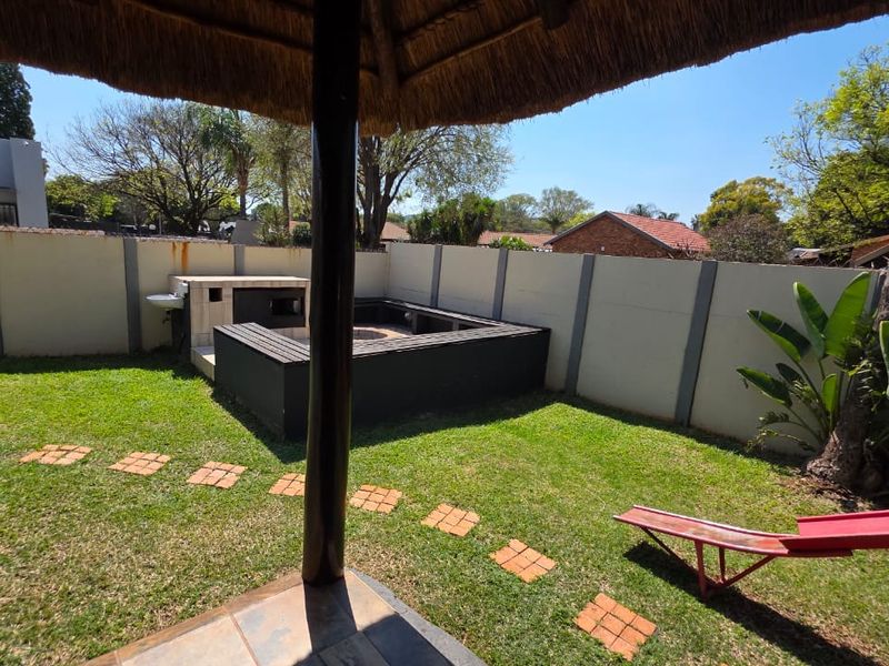 Private garden area featuring a built-in braai, outdoor sink, and a covered thatch patio area, enclosed by a perimeter wall.