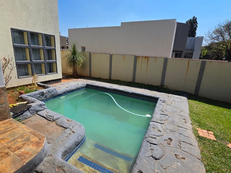 Outdoor pool area featuring a stone-edged swimming pool, a small lawn, and a perimeter wall with a built-in braai area.
