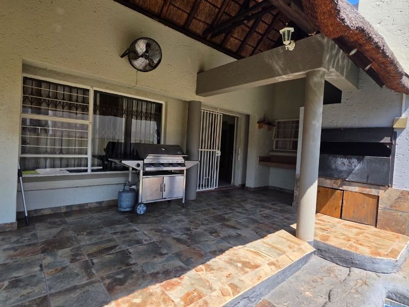Covered patio area featuring a built-in braai, stone tile flooring, and a thatched roof, providing a functional outdoor entertainment space.